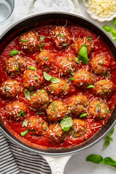 Zucchini meatballs in a skillet with marinara sauce, fresh basil, and parmesan cheese.