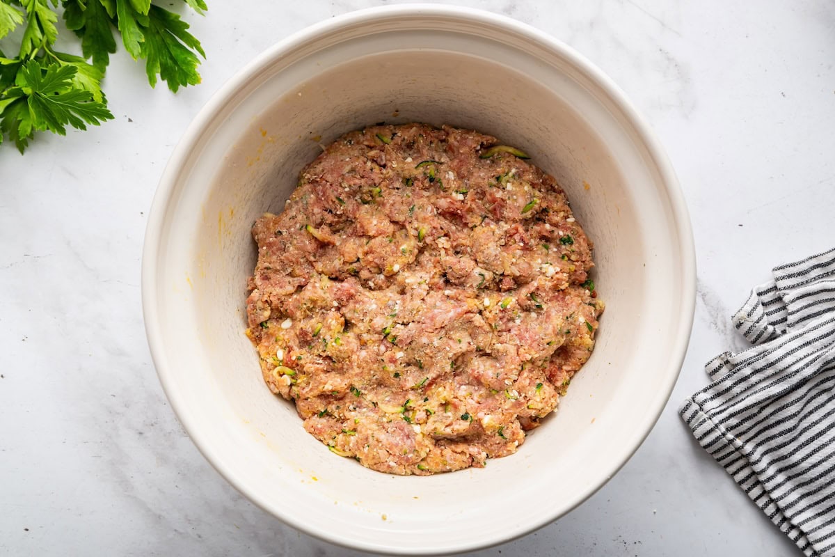 Seasoned ground beef in a large bowl used for zucchini meatballs.
