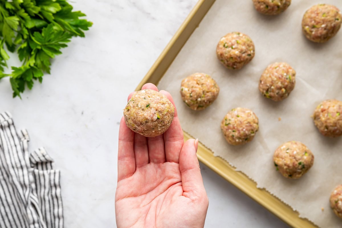 A hand holding a zucchini meatballs before being baked.