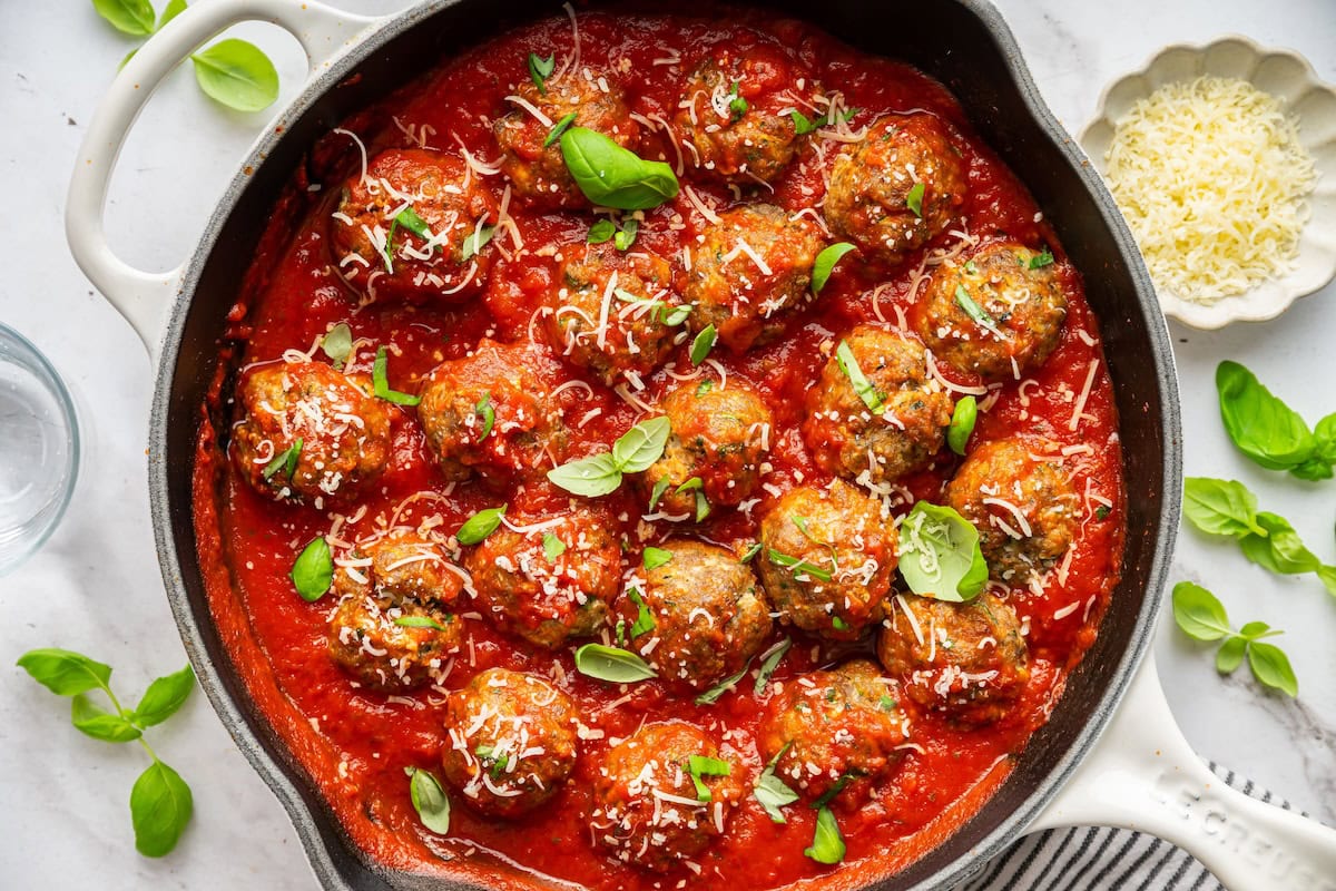 Baked zucchini meatballs in a skillet with marinara sauce, fresh basil, and parmesan cheese.