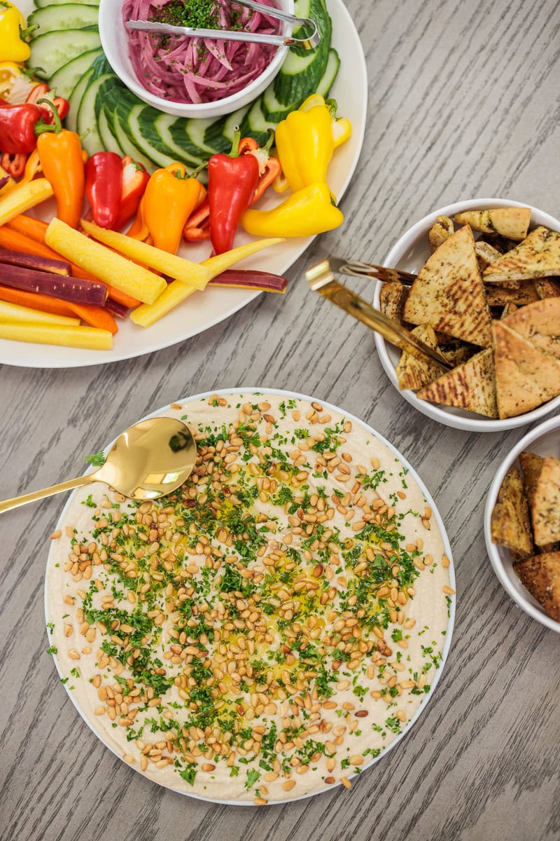 Hummus topped with pine nuts and herbs served with pita chips, vegetables, and pickled onions.