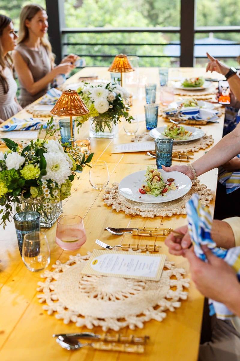 Fresh Air Retreat lunch table set with flowers, lamps, woven placemats, and plated salads.