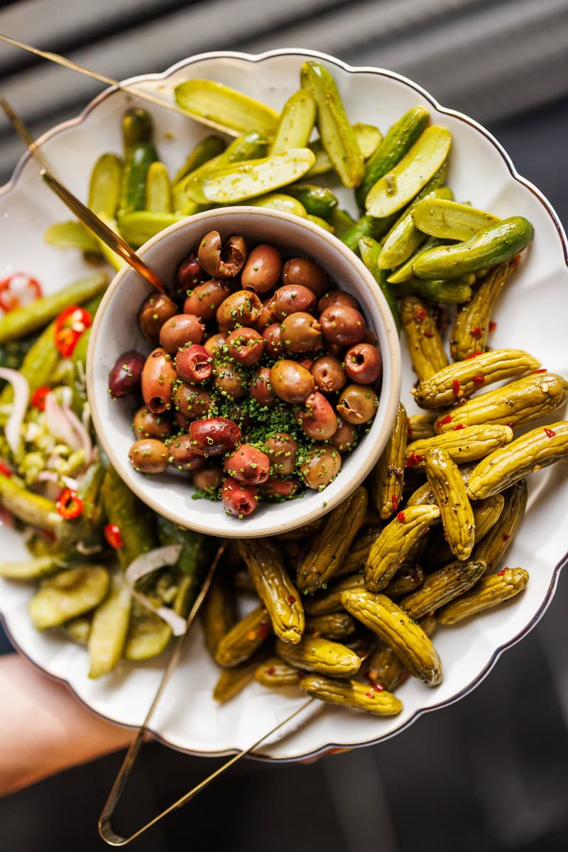 Assorted marinated pickles and olives served on a white plate.