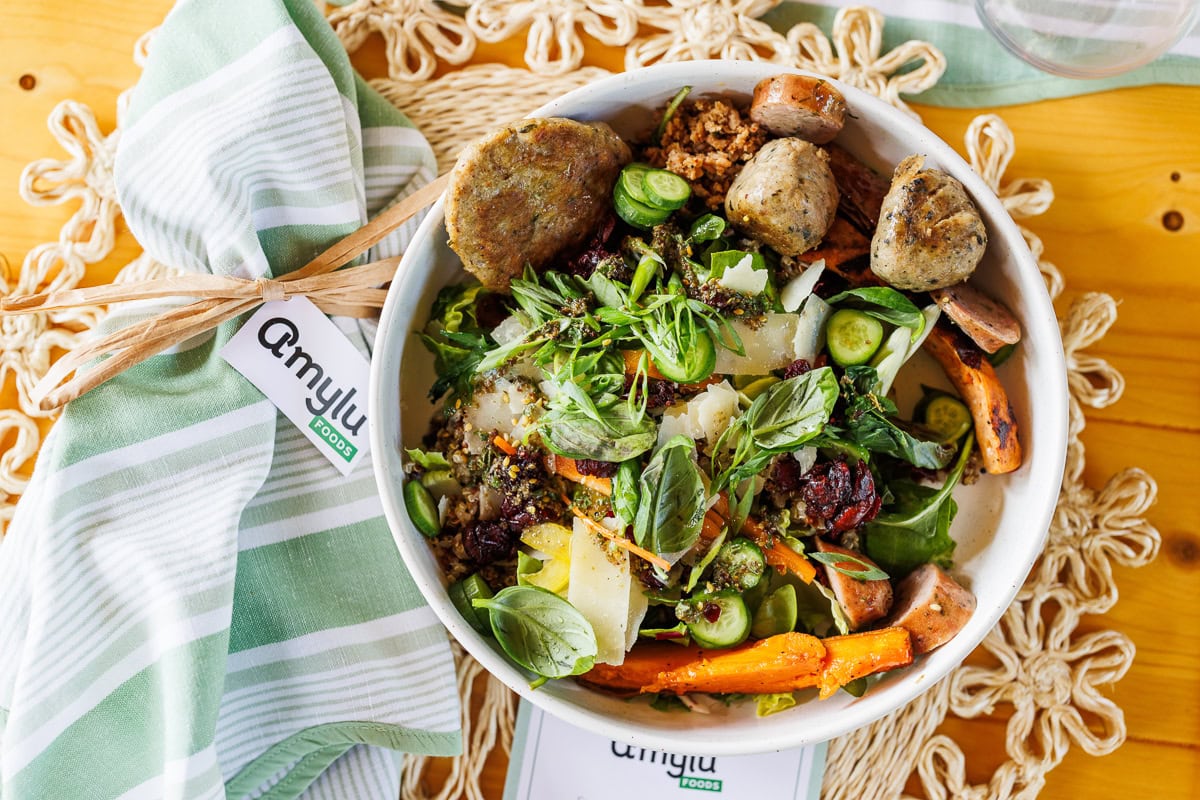 Amylu Foods salad bowl with chicken sausage, vegetables, greens, herbs, and shaved cheese.