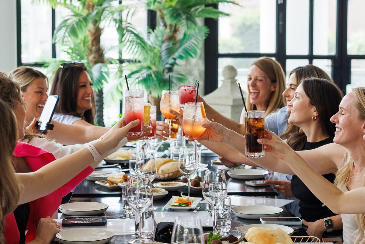 Group of women smiling and raising drinks during a shared meal.