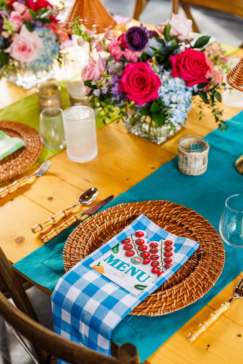Colorful table setting with woven plates, teal linens, flowers, and a printed menu.