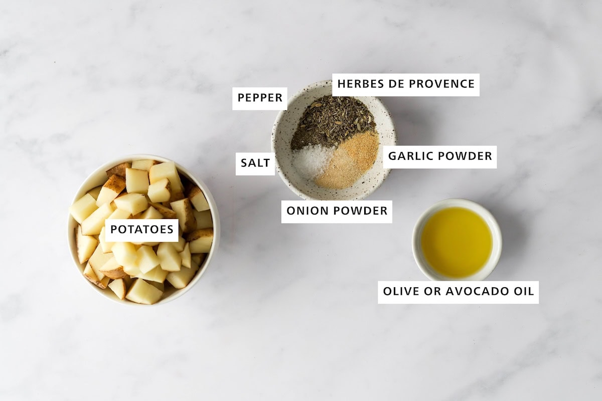 Ingredients measured out to make air fryer breakfast potatoes: potatoes, sea salt, pepper, herbes de provence/rosemary, onion powder, garlic powder and olive/avocado oil.