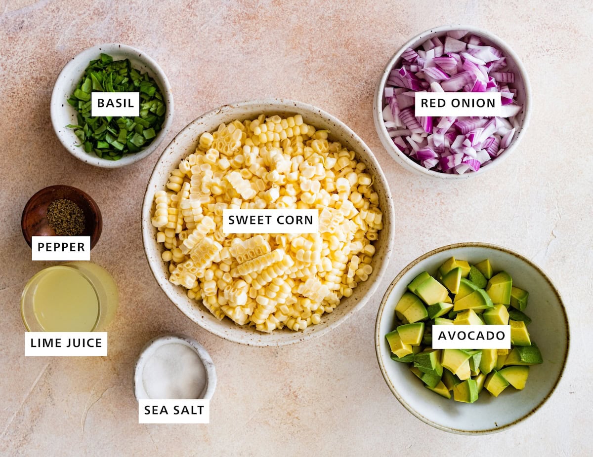 Ingredients measured out to make Avocado Corn Salad: red onion, avocado, sweet corn, basil, pepper, lime juice and sea salt.