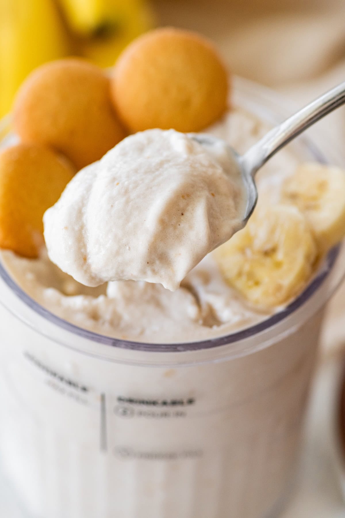 A spoonful of banana ice cream over a large container of the ice cream with vanilla wafers and banana slices to the side.