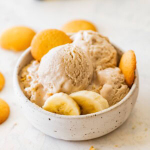High-protein banana ice cream served in a bowl with banana slices, and vanilla wafers on the side.