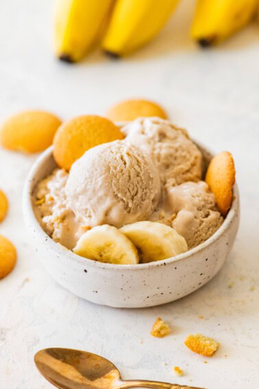 High-protein banana ice cream served in a bowl with banana slices, and vanilla wafers on the side.