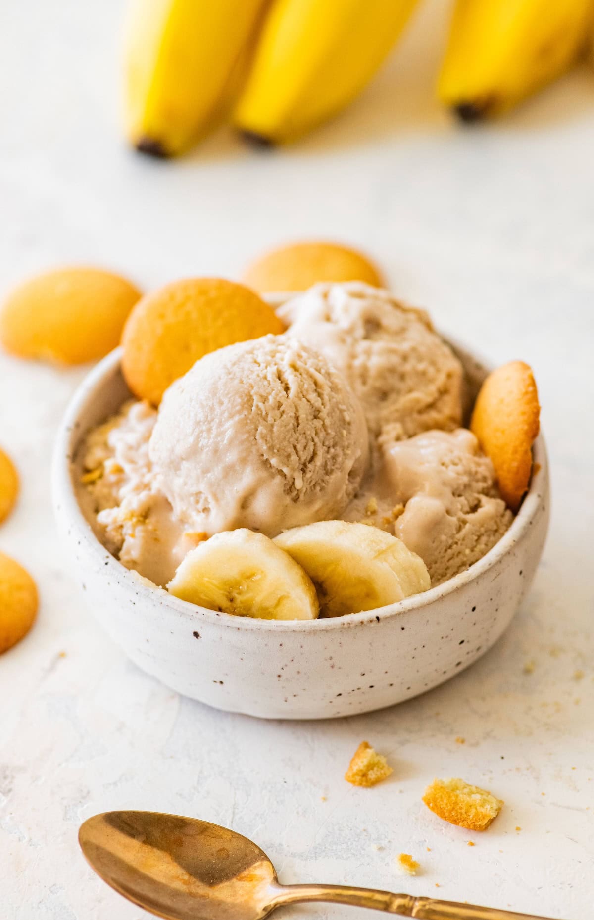 High-protein banana ice cream served in a bowl with banana slices, and vanilla wafers on the side.