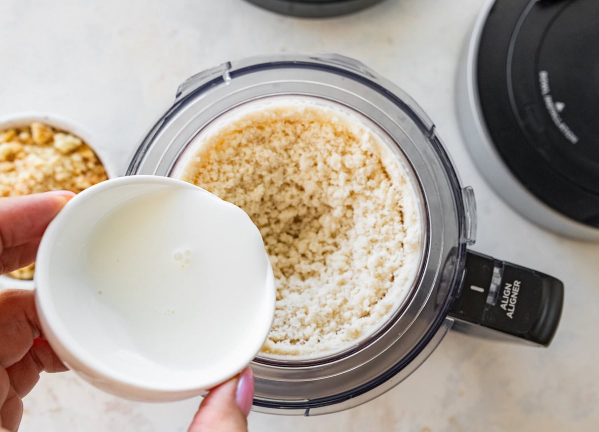 A hand pours a small amount of high-protein milk in a ninja creami with a mix of protein powder and banana inside.
