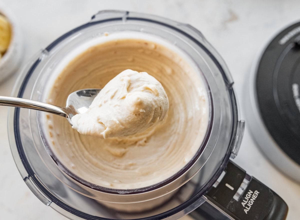 A spoonful of high-protein banana ice cream held over a ninja creami full of the ice cream.
