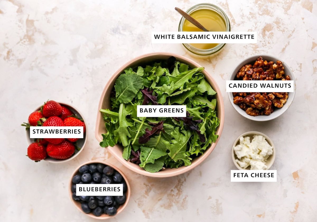Ingredients measured out to make Summer Berry Salad with Maple Walnuts: strawberries, blueberries, baby greens, white balsamic dressing, cheese and candied walnuts.