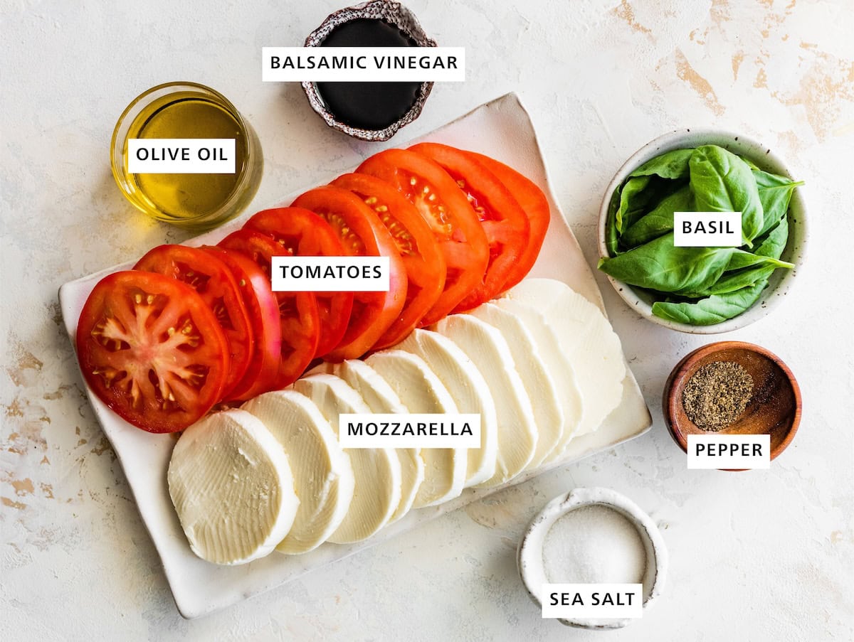 Ingredients measured out to make Easy Caprese Salad: fresh basil, pepper, sea salt, balsamic vinegar, fresh mozzarella, tomatoes and olive oil.