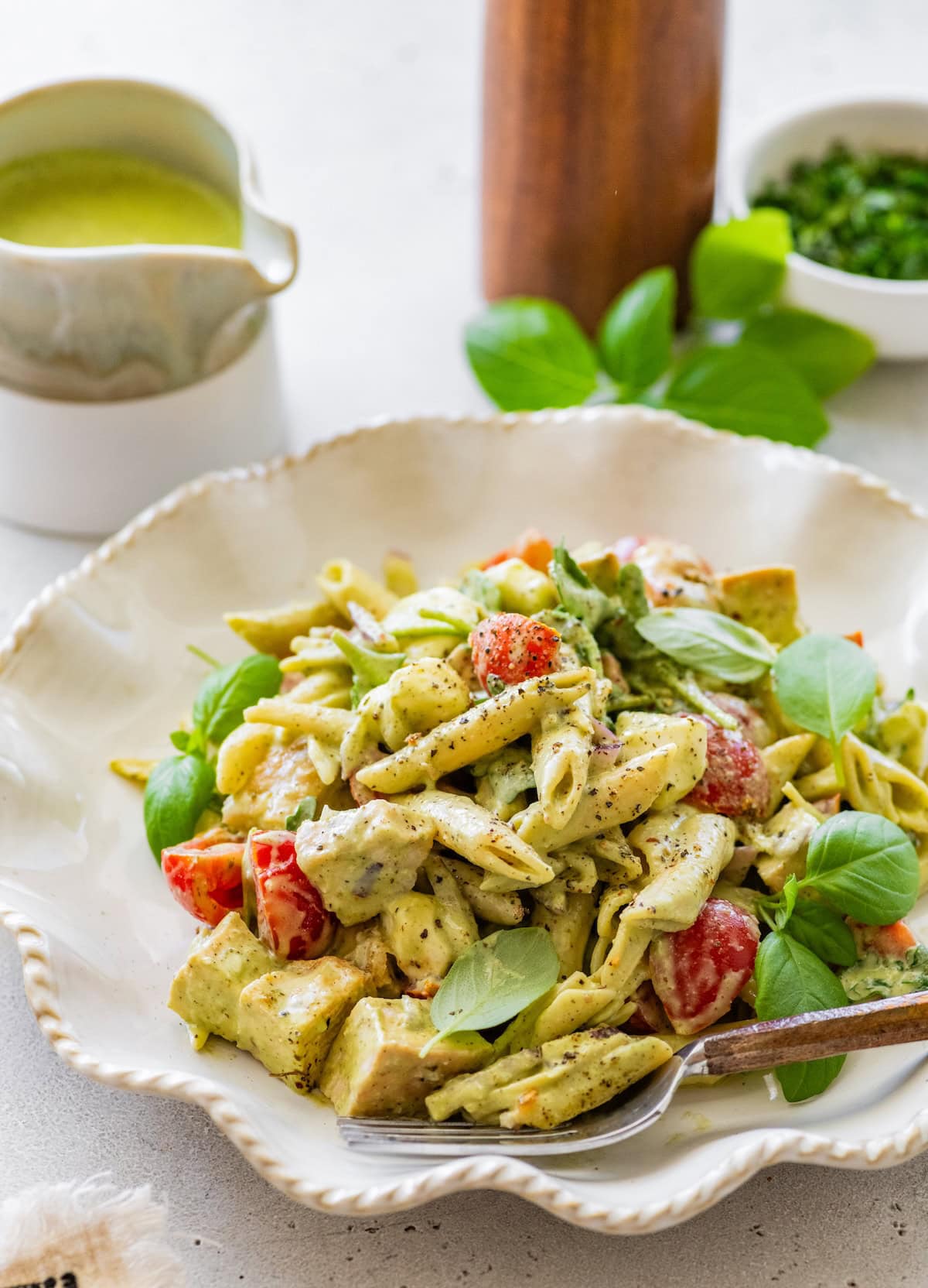 Chicken pesto pasta salad garnished with fresh basil leaves served in a shallow bowl.
