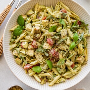 Chicken pesto pasta salad garnished with fresh basil in a large serving bowl.