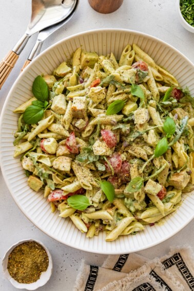 Chicken pesto pasta salad garnished with fresh basil in a large serving bowl.