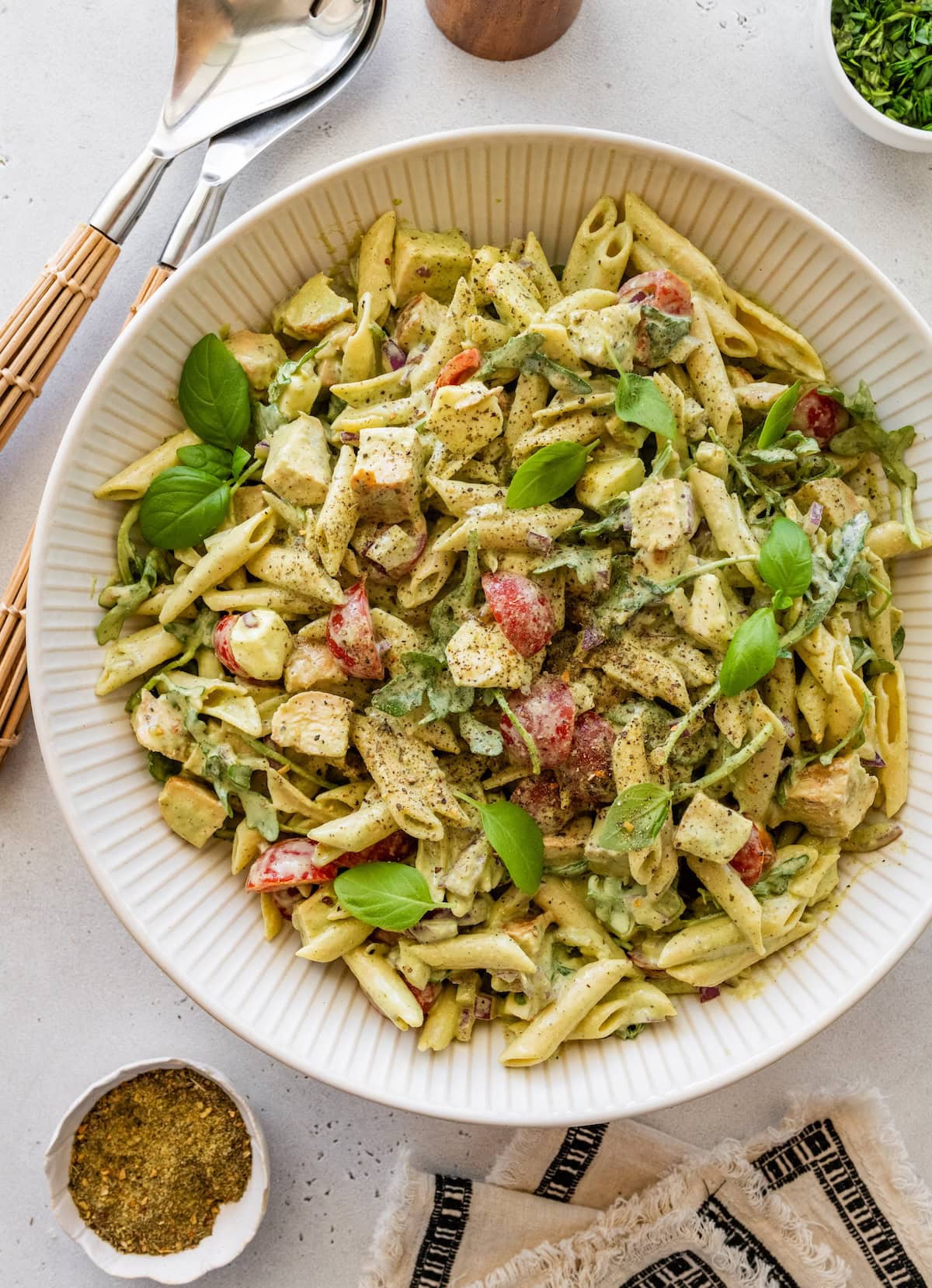 Chicken pesto pasta salad garnished with fresh basil in a large serving bowl.