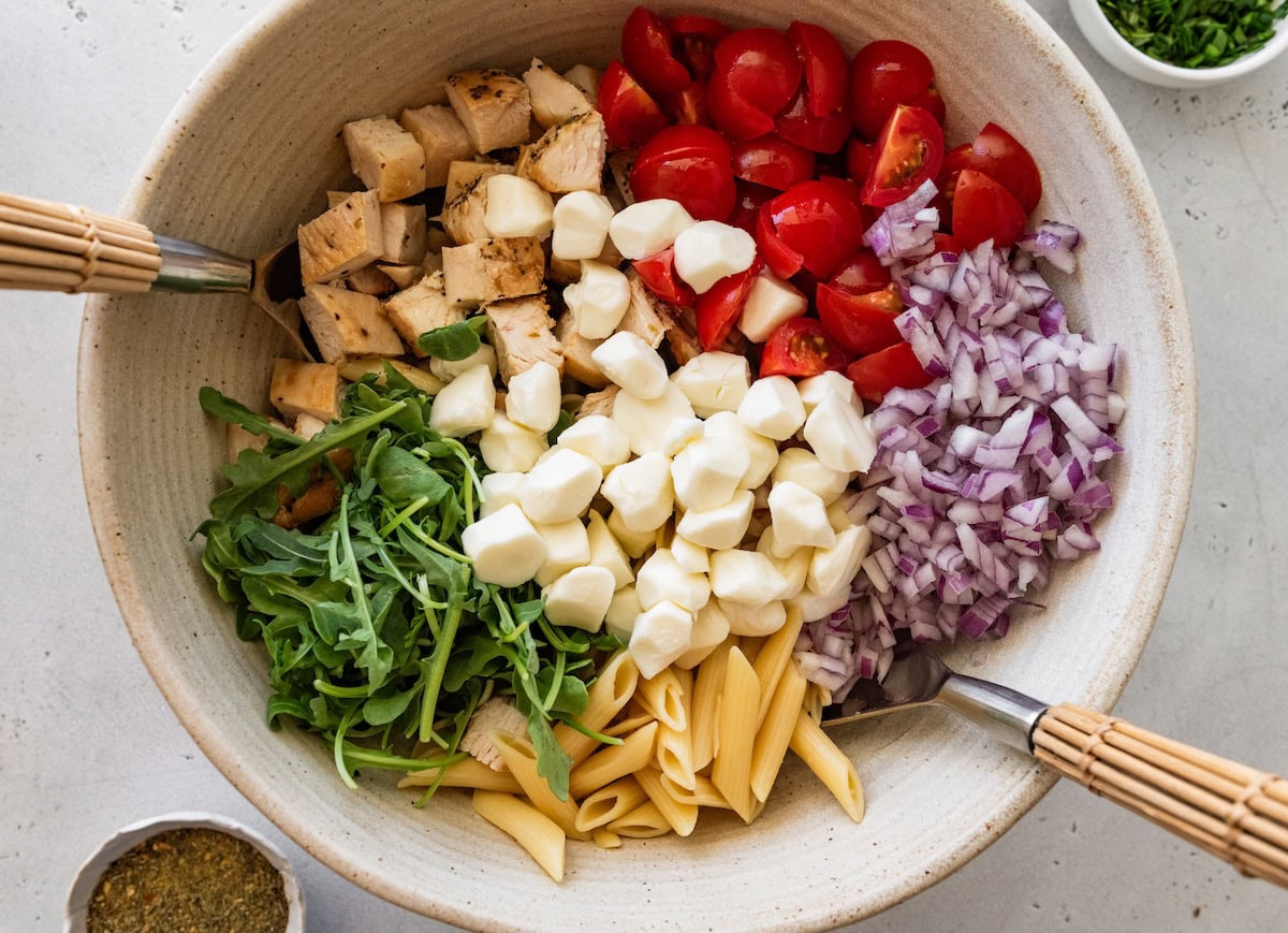 Ingredients for chicken pesto pasta salad separated in a large mixing bowl.