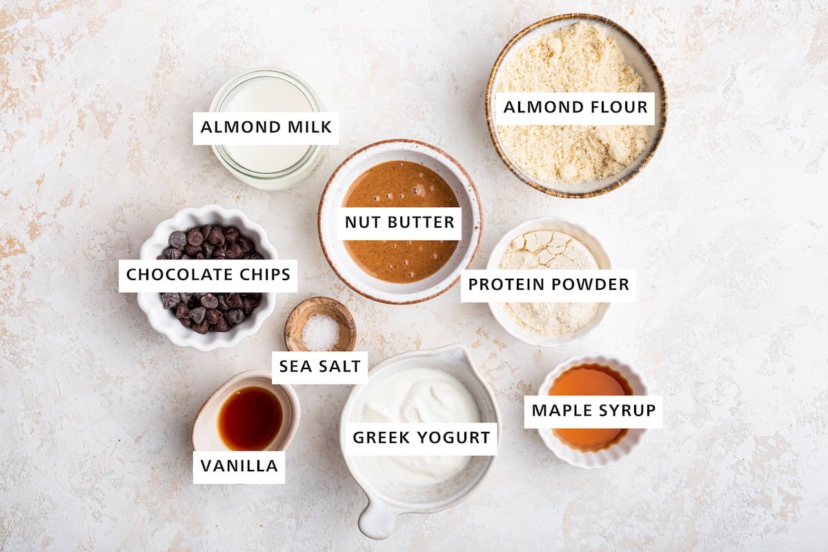 Ingredients measured out to make Protein Cookie Dough: almond flour, vanilla protein powder, maple syrup, almond/cashew/peanut butter, Greek yogurt, almond milk, sea salt, vanilla and chocolate chips.