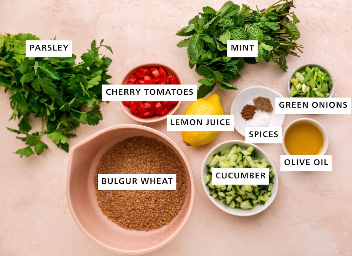 Ingredients measured out to make a tabbouleh salad: parsley, bulgur wheat, cherry tomatoes, lemon juice, allspice, cucumber, mint, salt, pepper, olive oil, green onions.