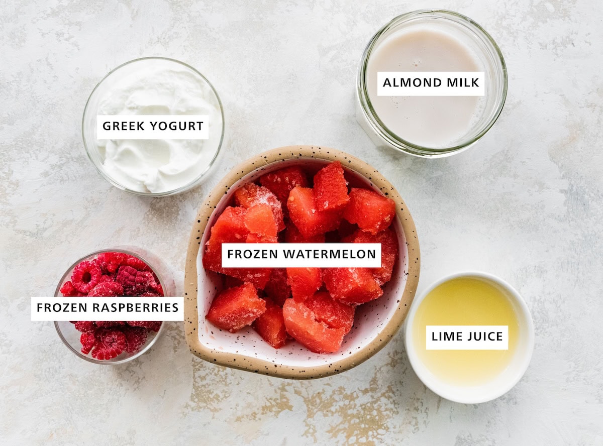 Ingredients measured out to make a Watermelon Smoothie: almond milk, lime juice, frozen watermelon, plain Greek yogurt and frozen raspberries.