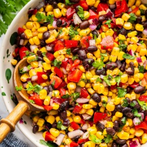 A large bowl with a black bean and corn salad recipe with a large wooden serving spoon.