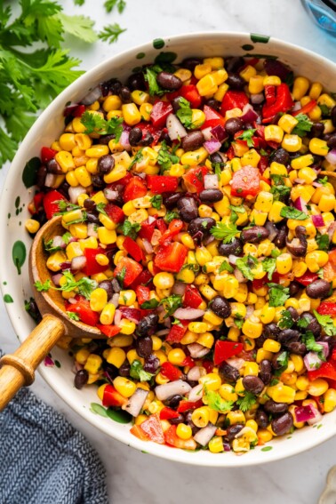 A large bowl with a black bean and corn salad recipe with a large wooden serving spoon.