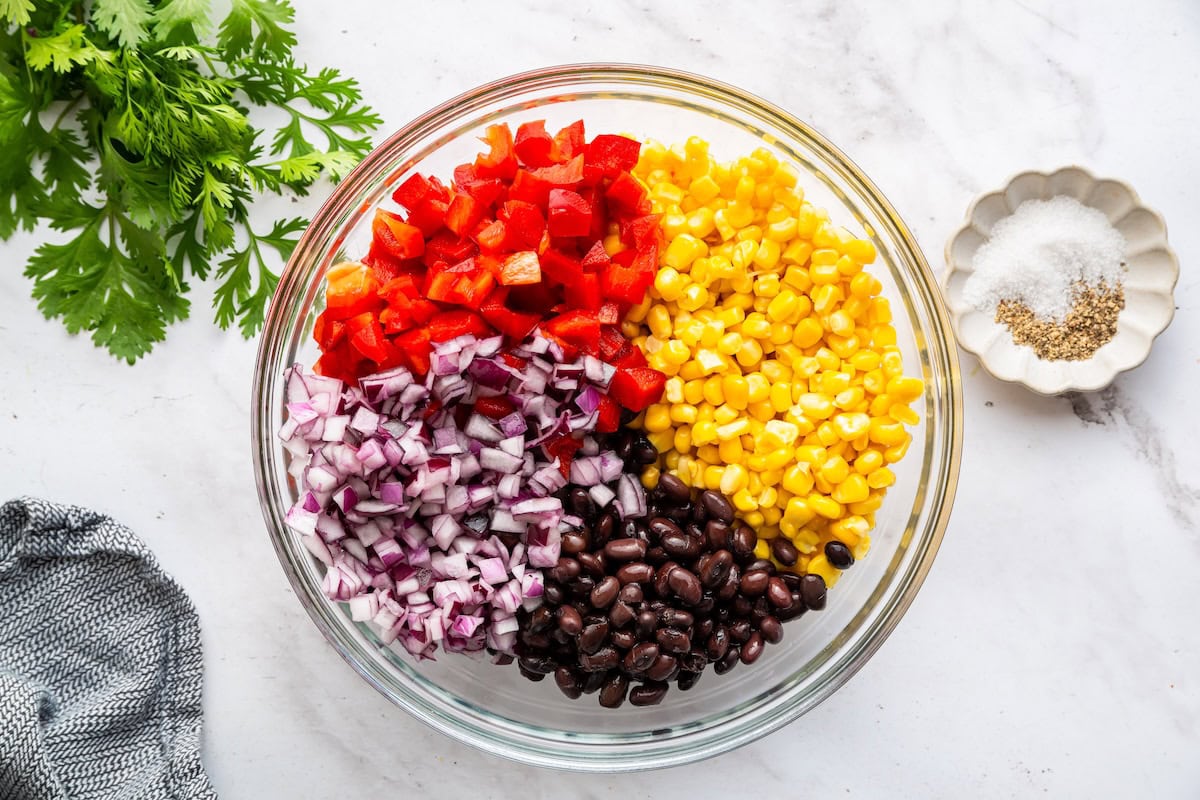 Corn, black beans, red onion, and red bell pepper in a large glass bowl.