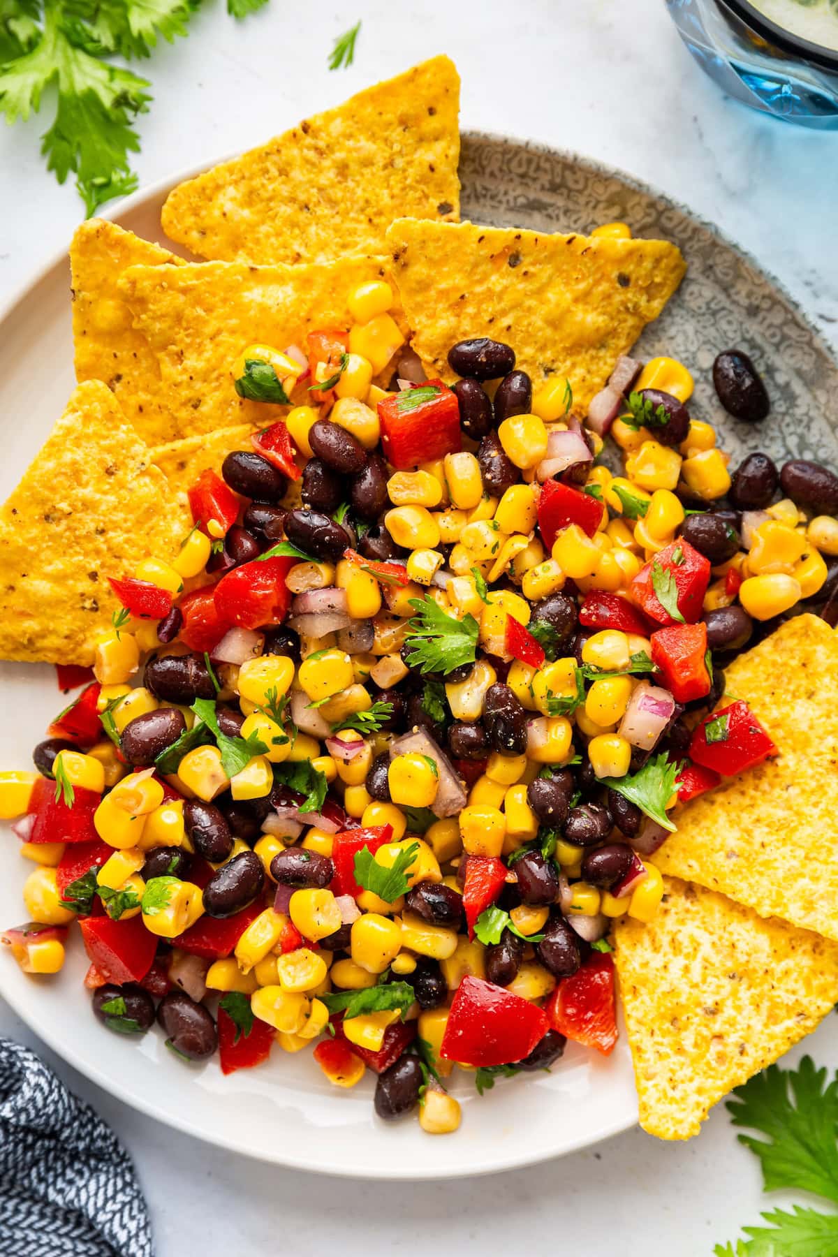 A serving of black bean and corn salad on a plate with tortilla chips on the side.