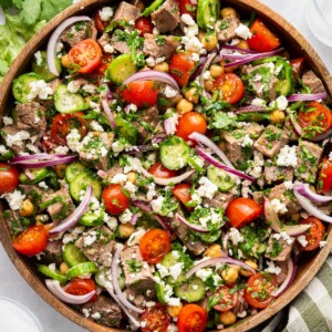 Chimichurri steak salad in a large wooden bowl garnished with feta and cilantro.