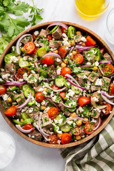 Chimichurri steak salad in a large wooden bowl garnished with feta and cilantro.