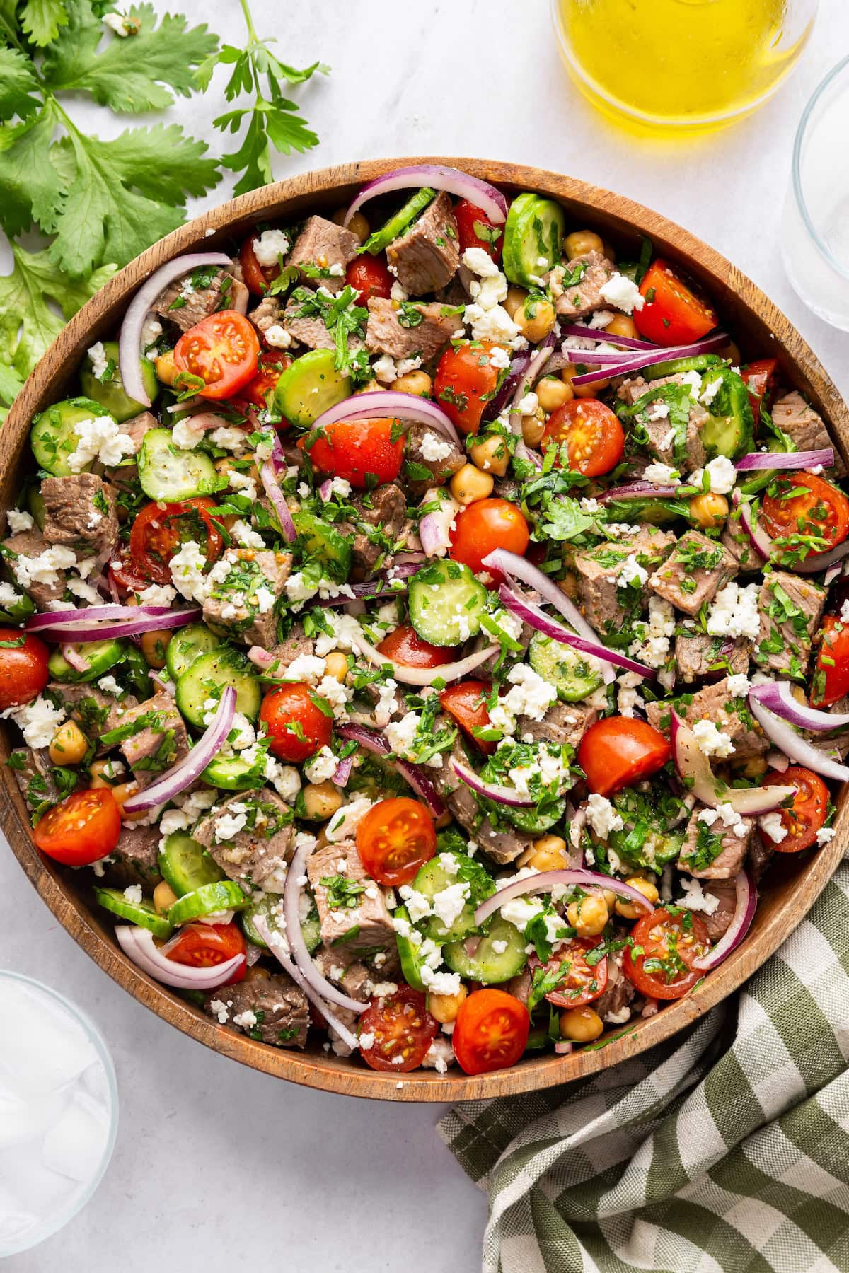 Chimichurri steak salad in a large wooden bowl garnished with feta and cilantro.