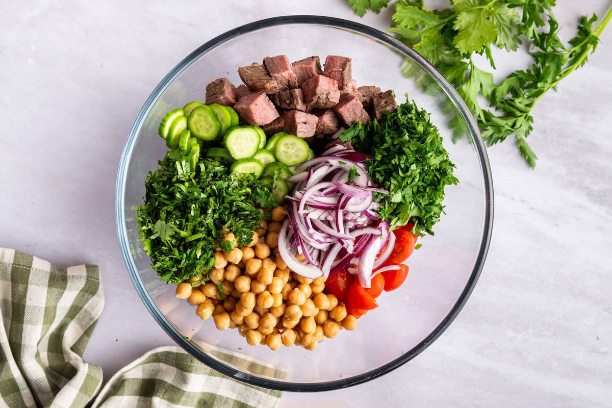 A large glass bowl with ingredients used for a chimichurri steak salad.