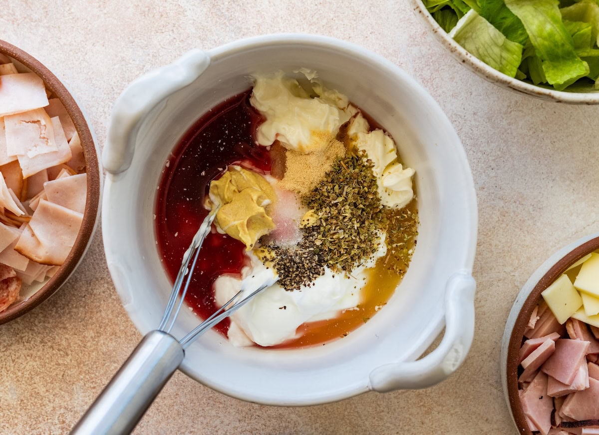 Ingredients used for a salad dressing in a bowl with a metal whisk.