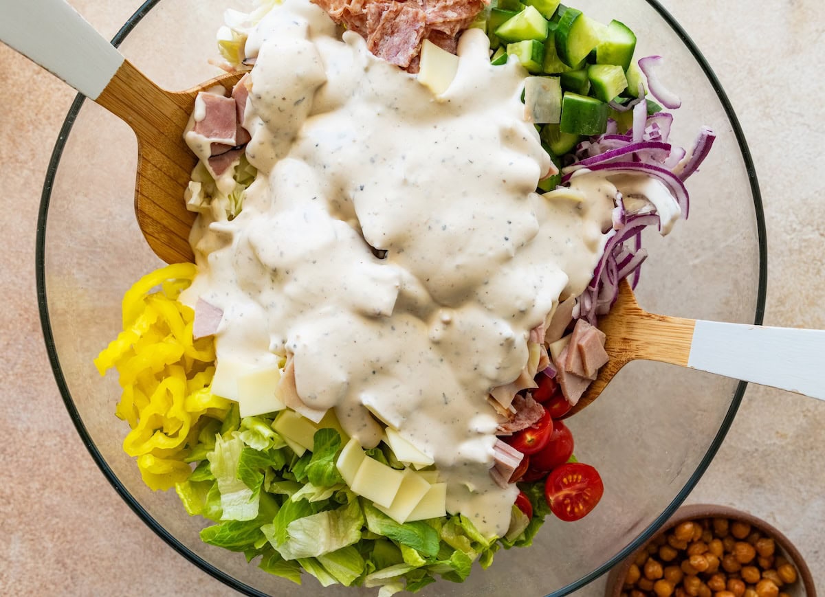 Dressing added to a large glass bowl of grinder salad ingredients.