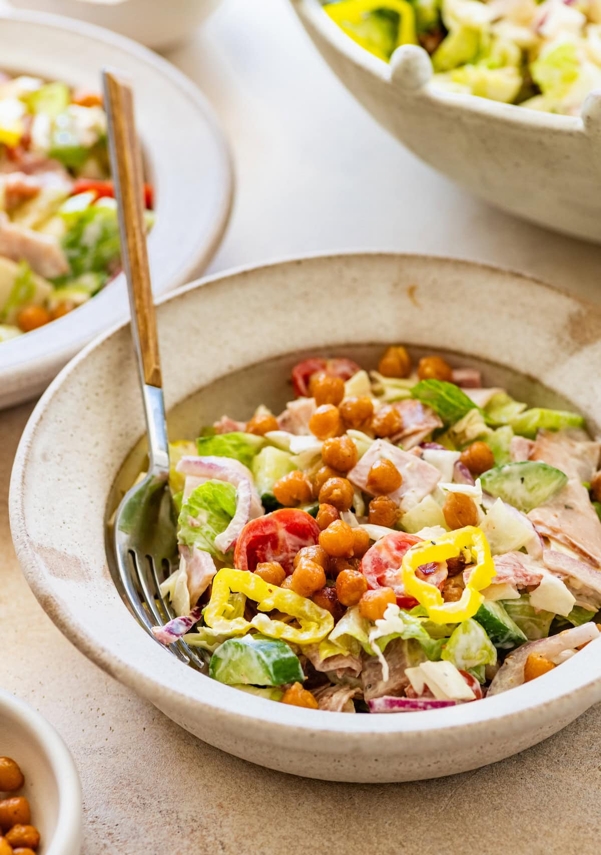 A serving of grinder salad in a bowl with fresh veggies, chickpeas, and deli meats.