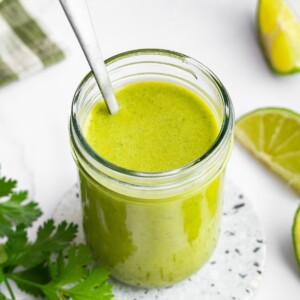 Cilantro lime dressing in a glass mason jar with a metal spoon in the jar of dressing.