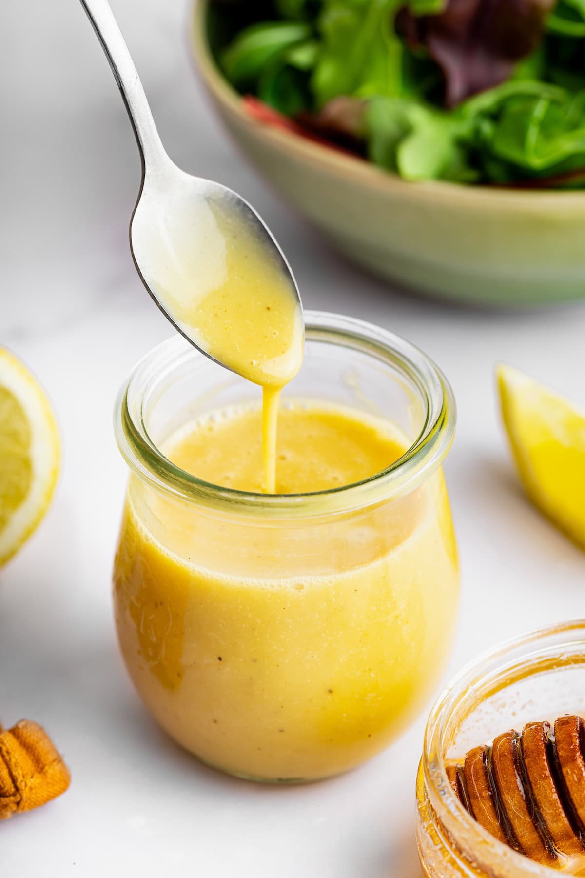 A spoon with a drizzle of honey mustard dressing over a glass jar of the dressing.