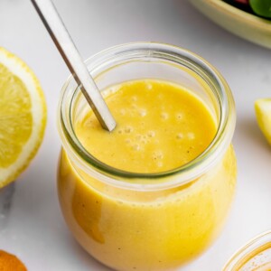 A honey mustard salad dressing in a glass jar with a metal spoon.