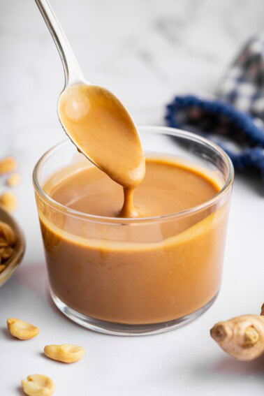 A peanut dressing in a glass cup with a metal spoon being lifted from the cup.