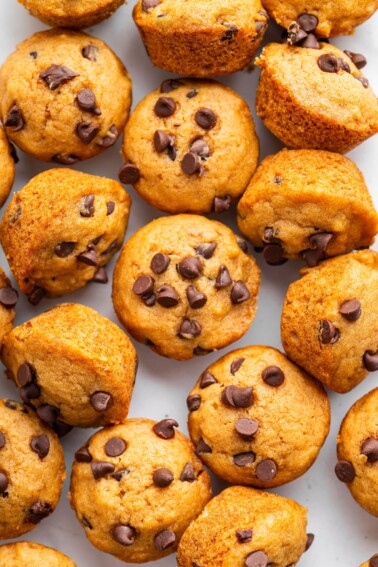 Mini chocolate chip muffins on a table close to one another.