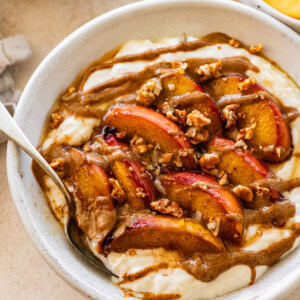 A serving of a peach crisp protein packed yogurt bowl topped with granola and a drizzle of almond butter.