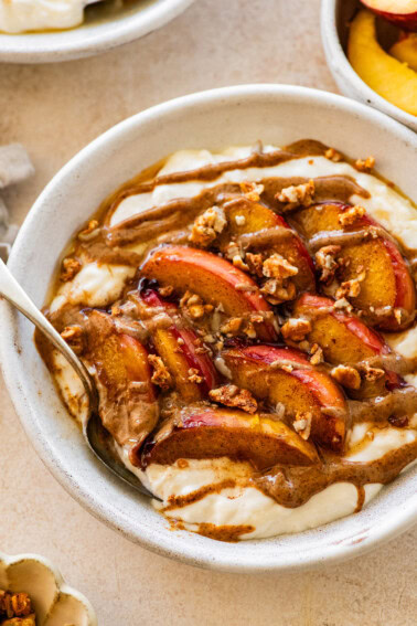 A serving of a peach crisp protein packed yogurt bowl topped with granola and a drizzle of almond butter.