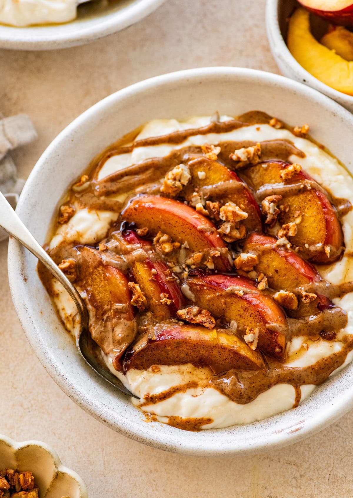 A serving of a peach crisp protein packed yogurt bowl topped with granola and a drizzle of almond butter.