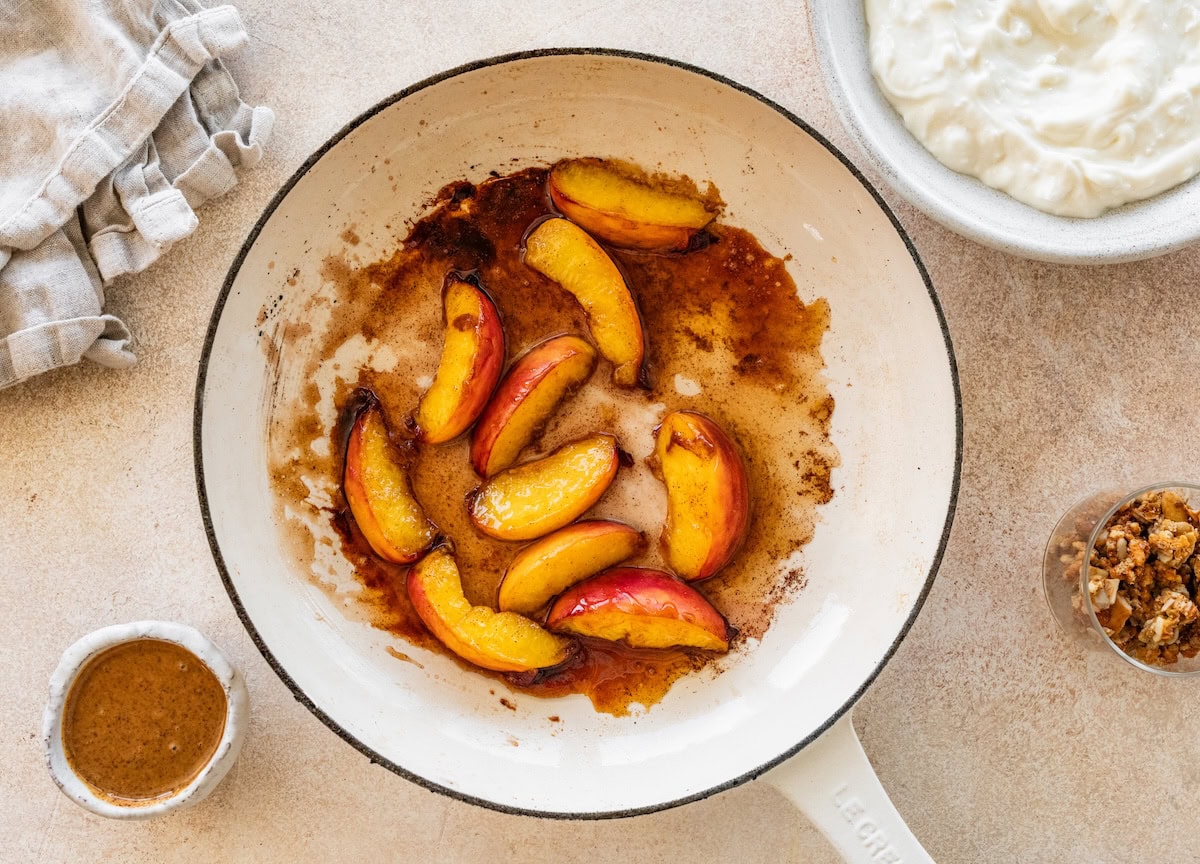 Sliced peaches in a skillet with maple syrup.