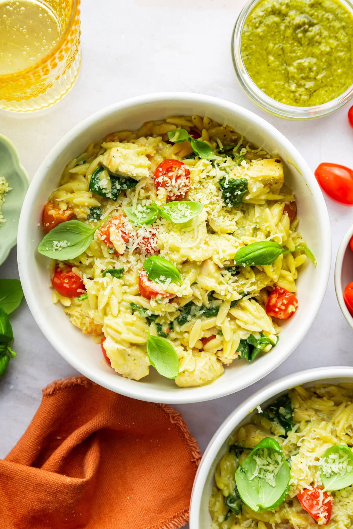 A serving of pesto chicken and orzo in a bowl topped with fresh basil and parmesan cheese.