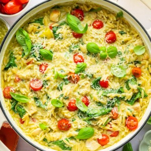 A large pot of pesto chicken, orzo, cherry tomatoes, spinach, parmesan cheese, and fresh basil.